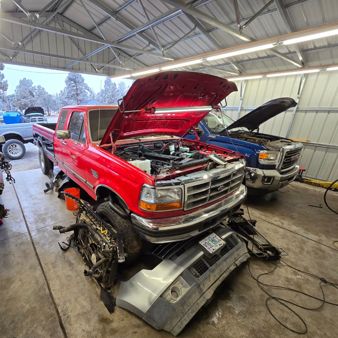 Red and blue pickup trucks with open hoods inside the BPE workshop in Bend.